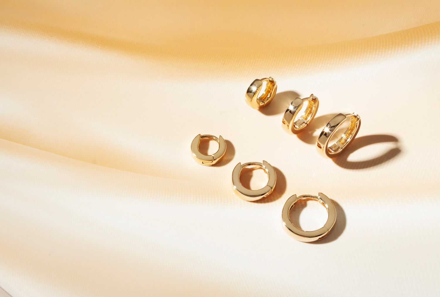 Three pairs of earrings sitting on top of a silk background.