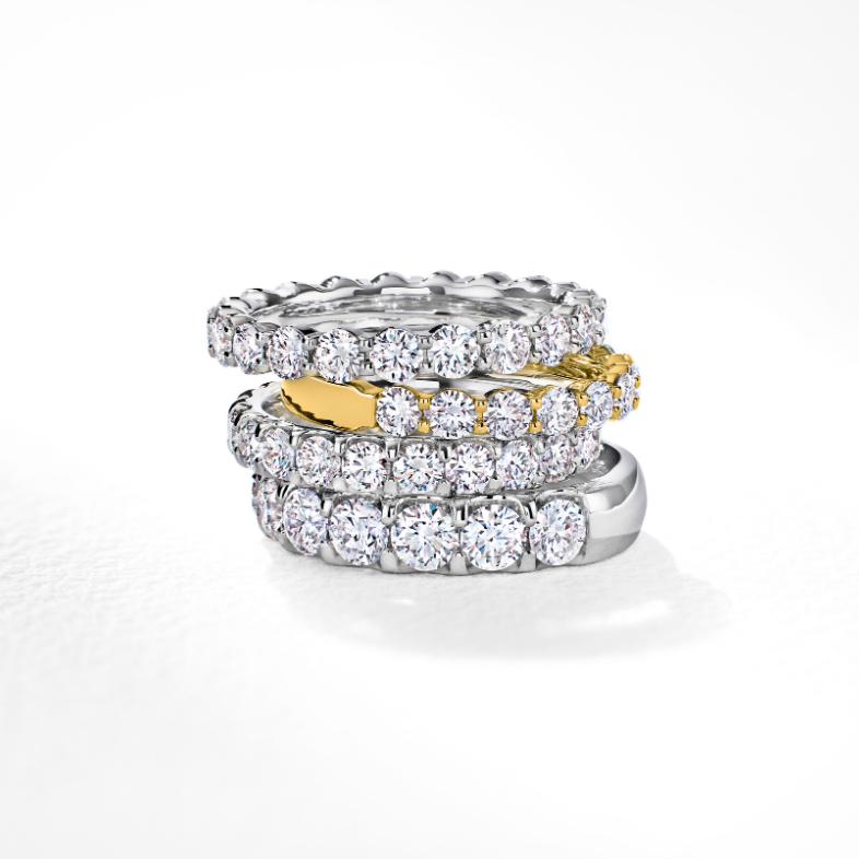 Stack of 4 diamond wedding bands with 3 white gold and one yellow gold against a white background