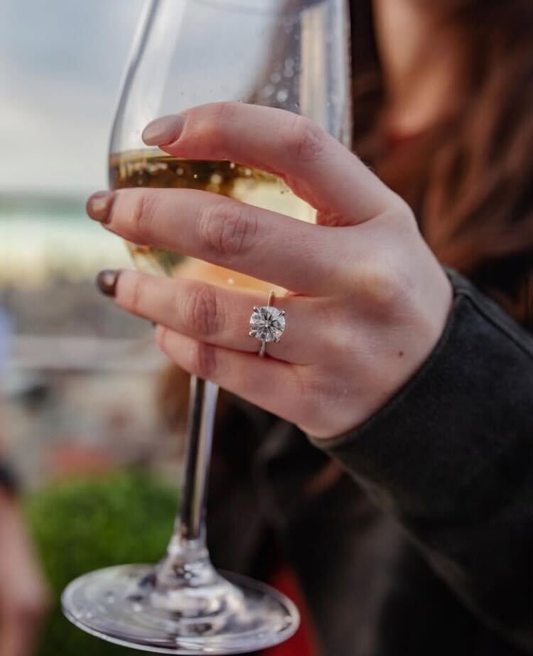 A woman's hand holding a wine glass, wearing a custom Holsten Jewelers engagement ring