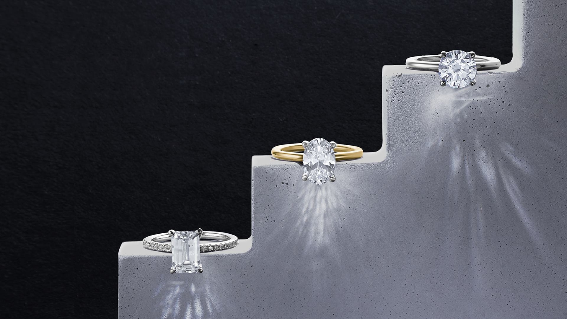 A concrete stairway display featuring a diamond engagement ring on each "step". Set against a black background.