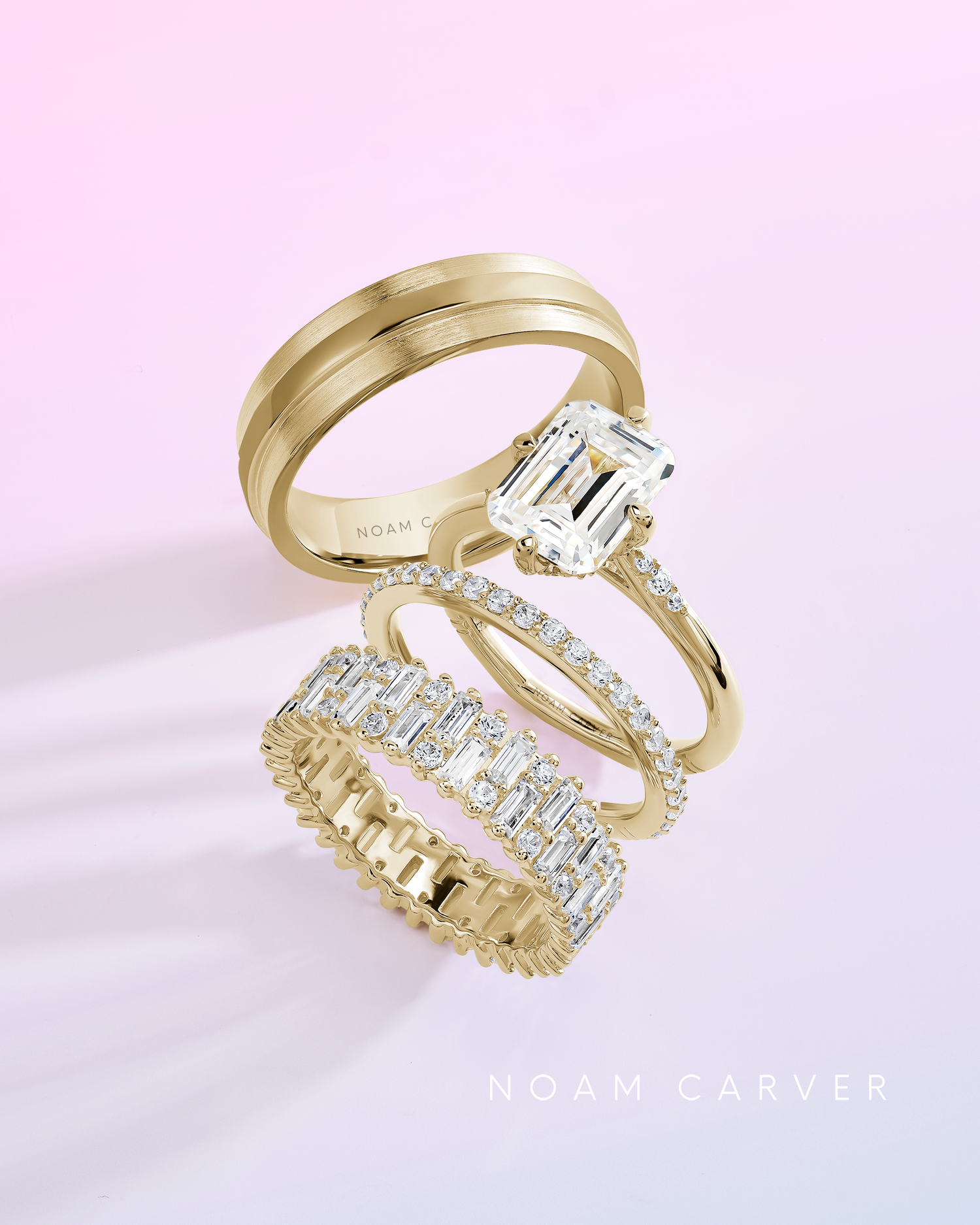 Four Naom Carver yellow gold rings (one engagement and three wedding bands) set against a light pink background