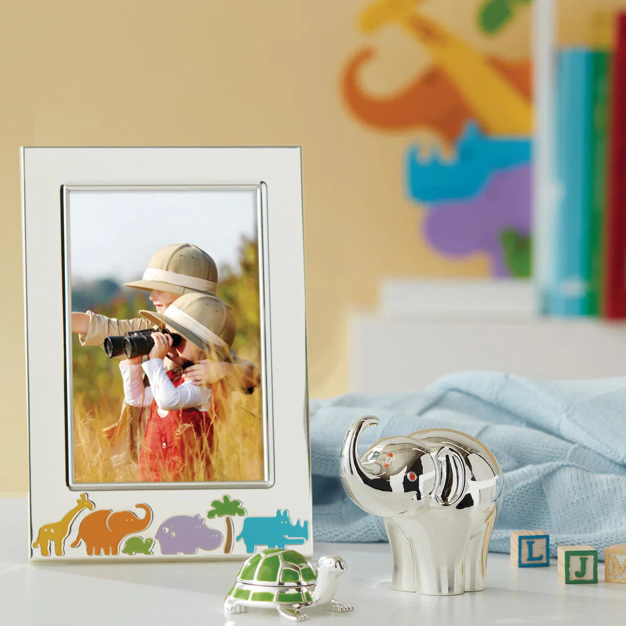 Silver frame with colorful animals on the bottom, next to a silver figurine of an elephant and turtle