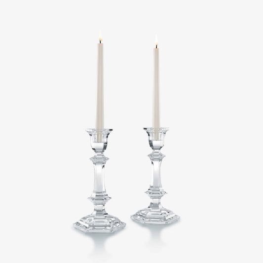 Two crystal candlestick holders with lit candles against a white background